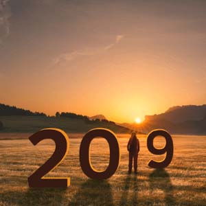 Person flanked by numbers to form "2019" standing in a field at sunrise