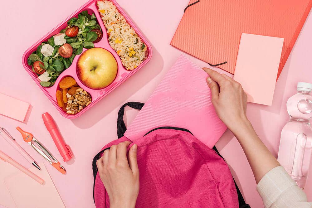 Person packing school supplies and a lunch into a backpack