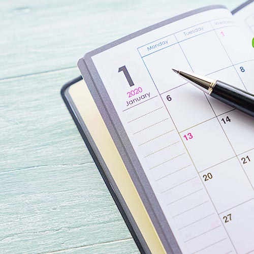 Monthly calendar planner with a pen resting on it on a background of white wooden boards