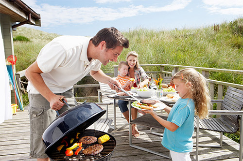 Family on vacation having barbecue sitting a deck near the beach