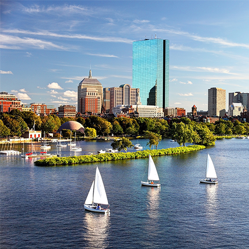 Skyline of Boston seen from over the ocean. Small ships in the foreground.