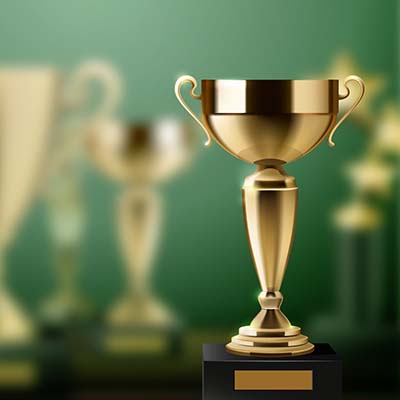 Golden trophies on a green background. One trophy is clear in the foreground, the rest are further from the camera and are out of focus