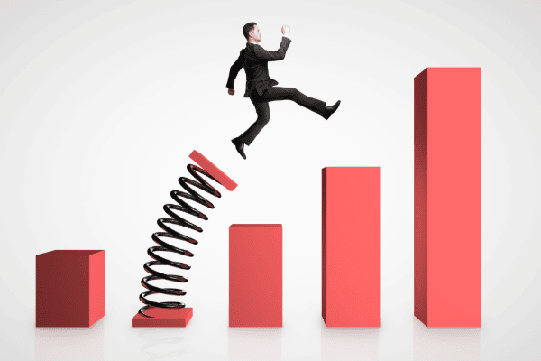 This graphic shows a series of red pillars of increasing height; the second pillar has turned into a spring and is launching a businessman forward.