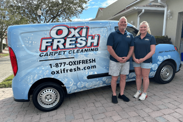 This image shows Will Chambers and his partner standing in front of their Oxi Fresh vehicle in blue polos and shorts.