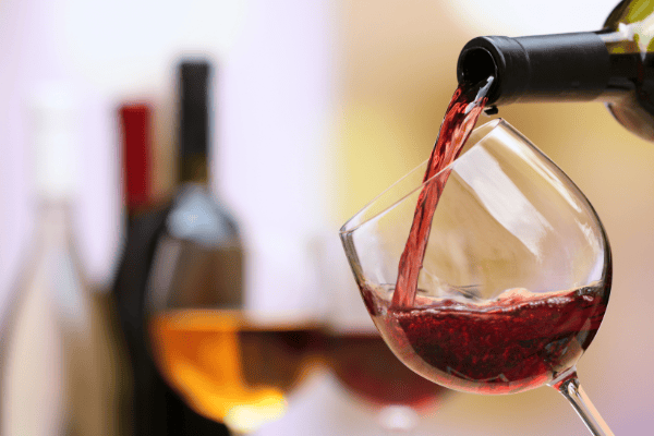 This square image features a glass of red wine being filled in the foreground, with more wine in the back.