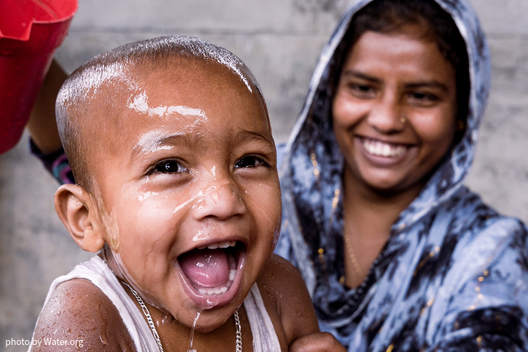 This image shows a mother splashing water on her laughing baby's head.