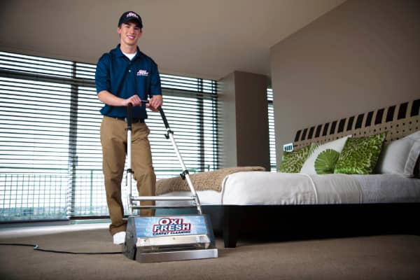 An Oxi Fresh technician stands with his carpet cleaning machine in a customer's bedroom.