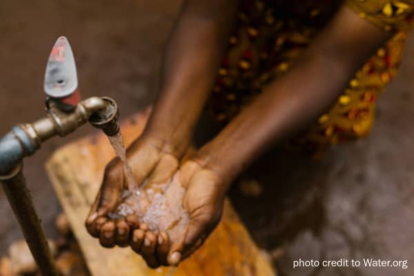 Water from a tap flows into a woman's cupped hands.