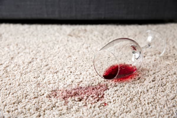 A glass of red wine spilled onto a light-colored carpet.