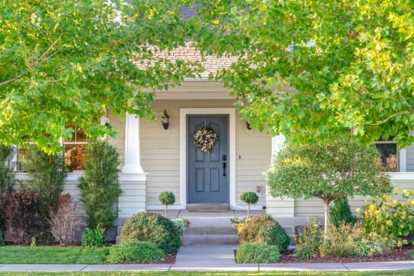 Front view of a small house shaded by green trees.