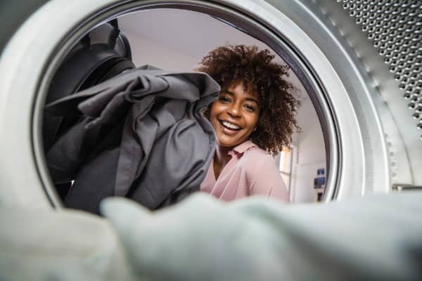A woman loads her dryer with clothes, as seen from inside the dryer.