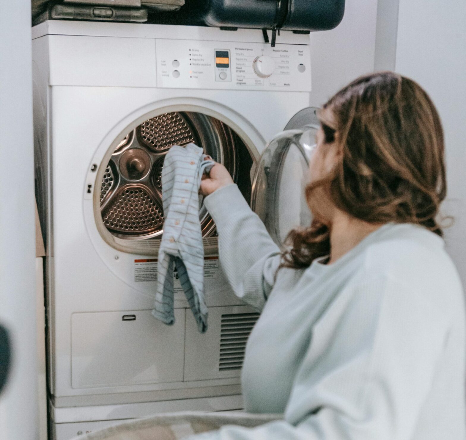 Woman holding a laundry basket and loading a dryer with laundry in a small laundry space.