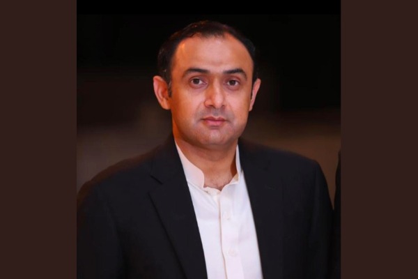 Oxi Fresh franchisee Malik Khar poses for a portrait in a dark suit against a dark background.